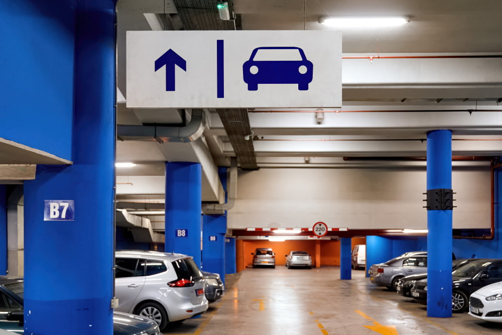 Spacious underground garage with blue pillars, parked cars, and an overhead sign showing a car symbol and arrow for guidance.