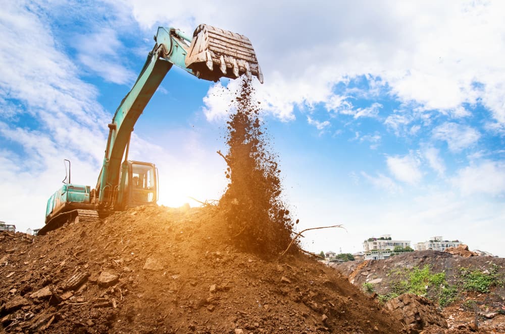 Excavator dumps soil under blue sky and white clouds, highlighting active construction and development.